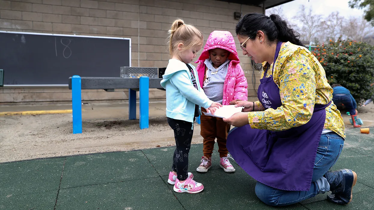 An educator outside the CSUSB Children’s Center speaking to two young children