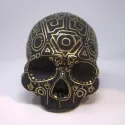 Half a skull painted in matte black with linear details in gold.