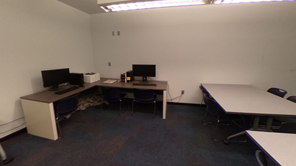 Student workspace with two desks chairs, corner desk with two monitors