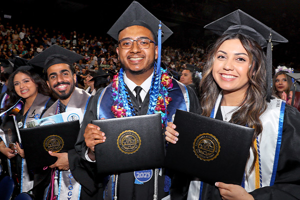 Graduates smile with diplomas at Spring 2023 Commencement