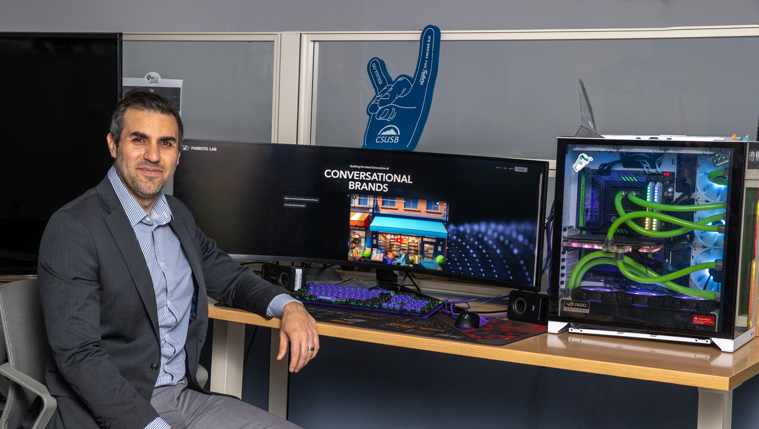Naja Faysal, who will finish a master’s degree in information systems technology degree in May 2024, strikes a pose in front of a computer showcasing the homepage of his AI company, Parrots Lab, LLC.