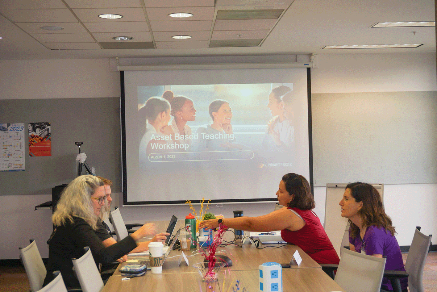 The image shows a table with teachers talking and working together