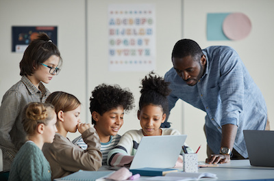 Teacher helping many students at laptop