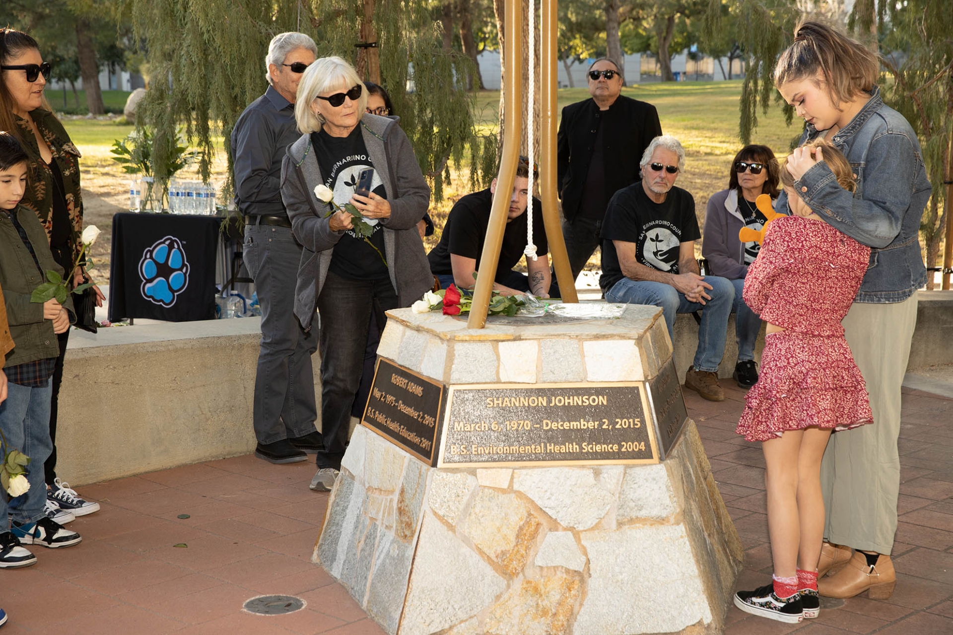 Family and friends leave roses on the base of the bell at the Peace Garden.