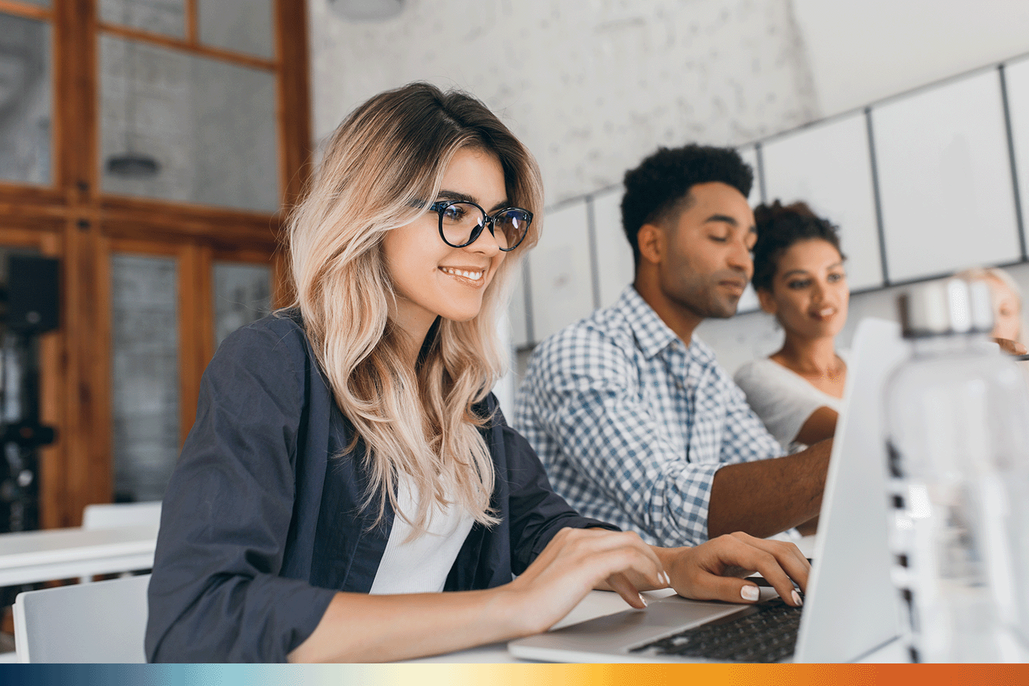 The image shows a curly haired female intern using a laptop and smiling next to a male and female coworker