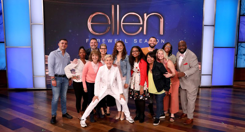 Reneisha S. Wilkes, sixth from the right, in the red sweater, and other guests with Ellen DeGeneres, standing in front wearing a white suit.