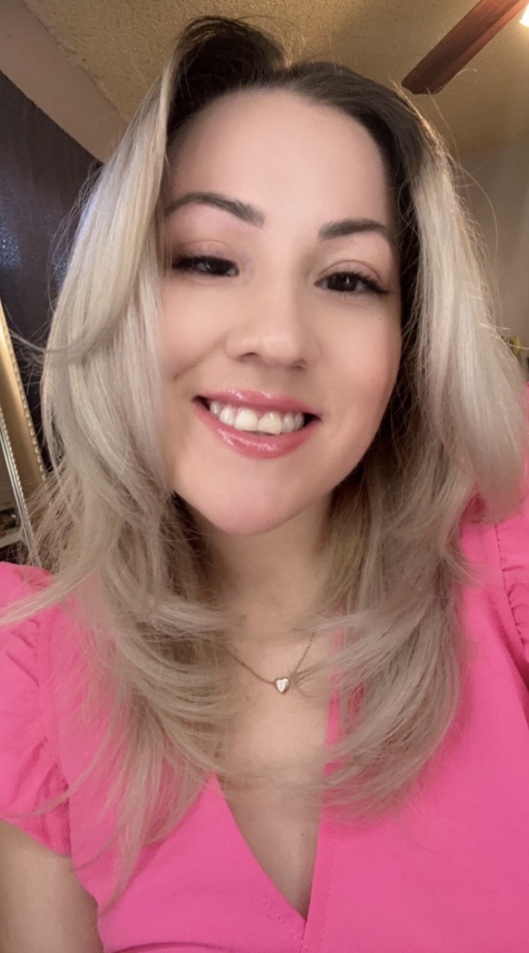 The Image shows Alexis Feliz. She has blonde hair and brown eyes. She has a professional pink blouse on and she is smiling.