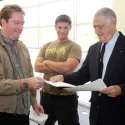 Three people standing two trading papers