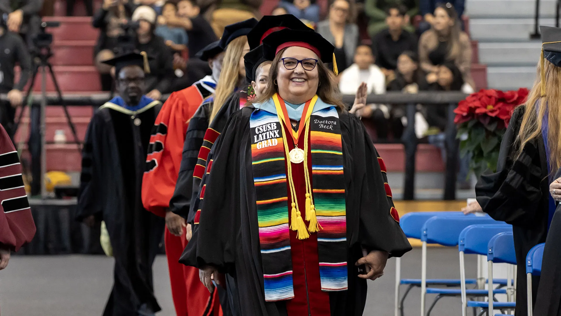 Carmen Beckin commencement regalia, walking at the front of a line of people.