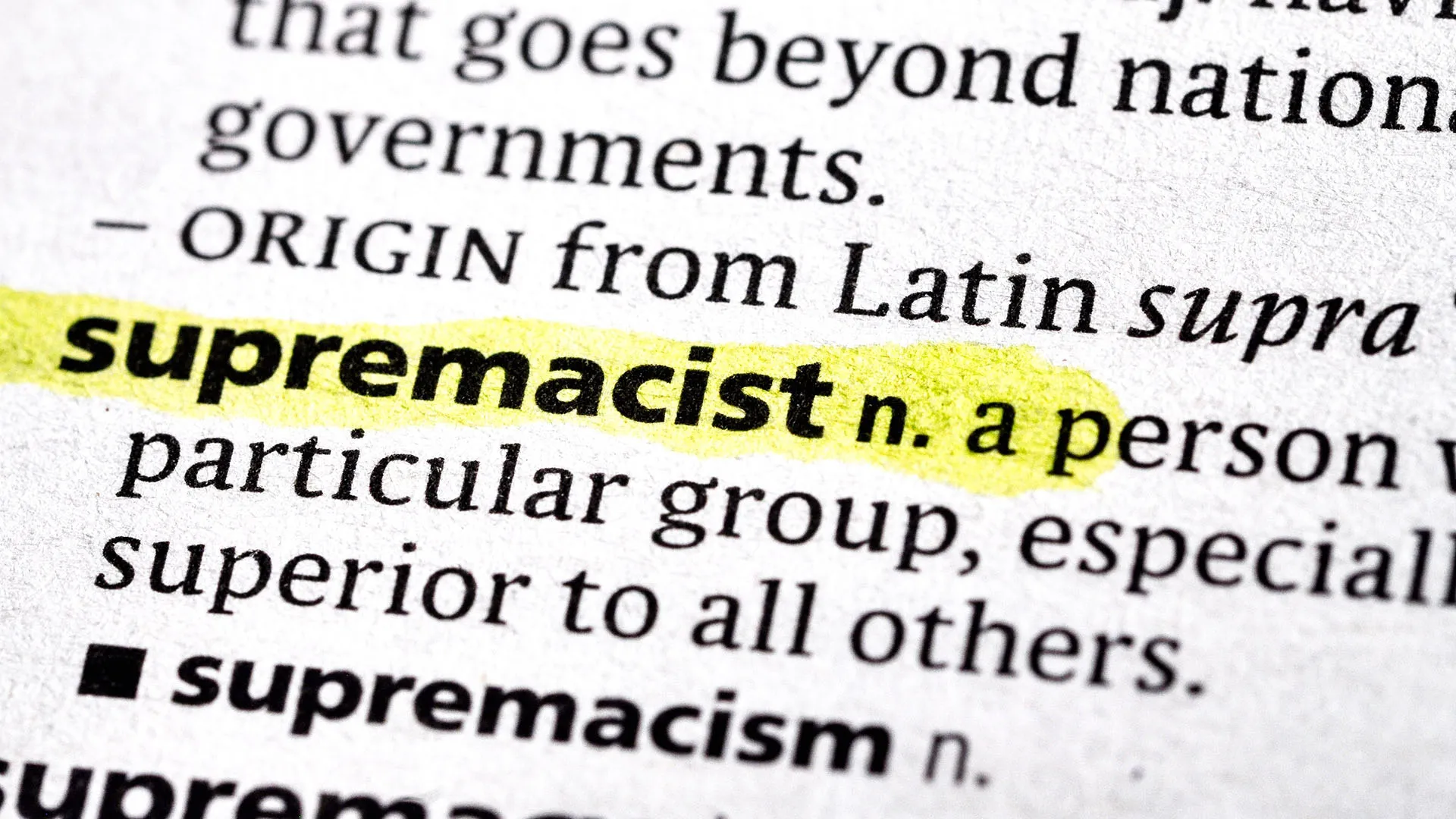 A close-up photograph of a dictionary entry for the word "supremacist," which is highlighted in yellow. The text surrounding it shows partial definitions for "supranational" above it and "supremacism" below it.