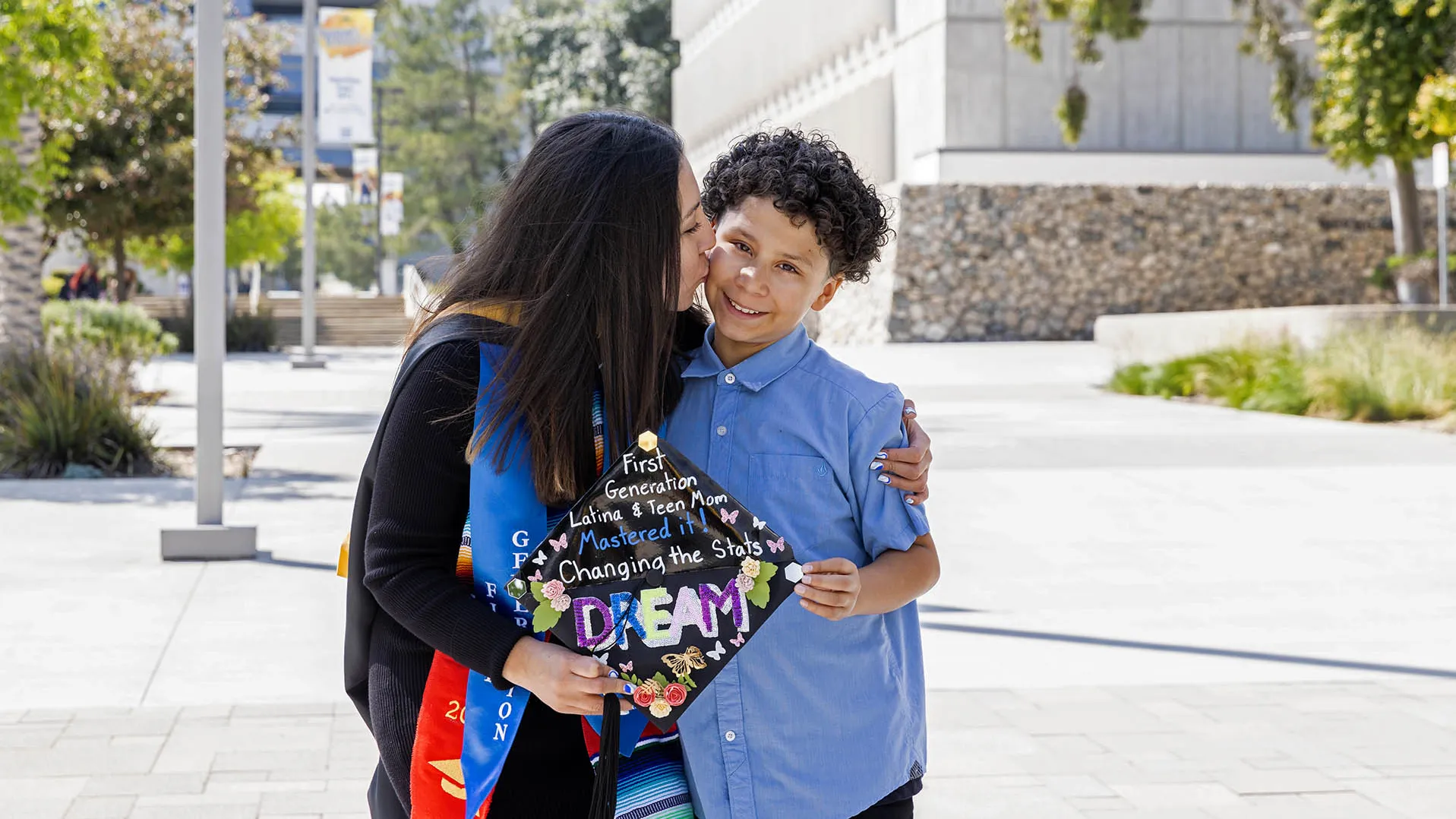Cristal Vasquez, Class of 2023, social work, in her cap and gown holding her mortarboard and her son.