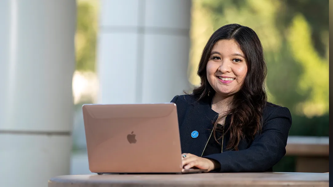 A student in front of Jack Brown Hall using her laptop