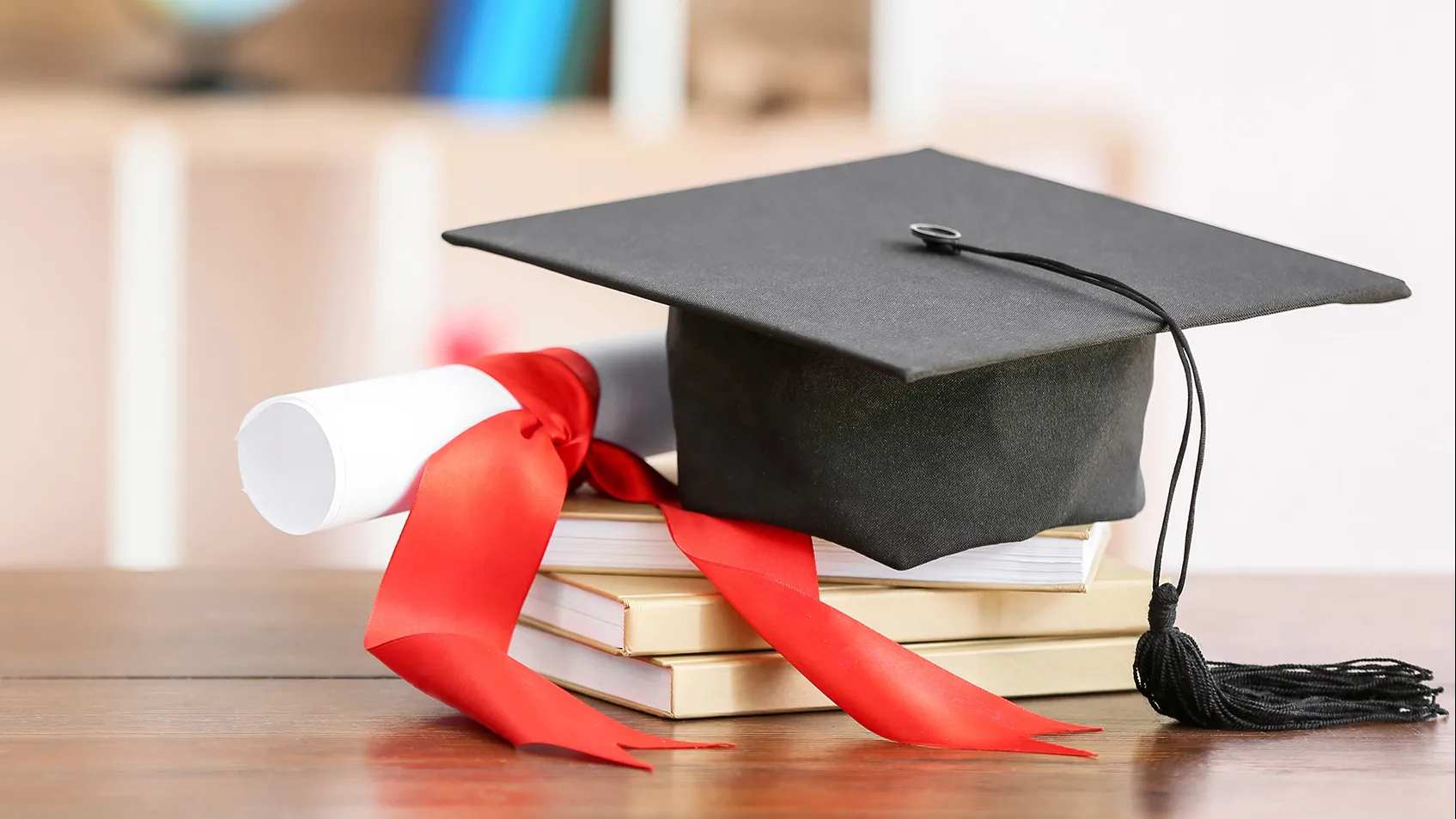 Photo of a mortarboard and rolled up paper and books illustrating education.