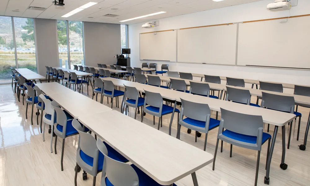 Classroom-style meeting space with rows of desks, a projector, and a podium for presentations.