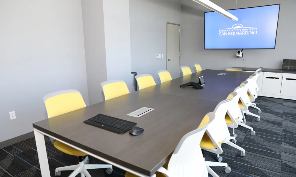 A spacious and modern boardroom with a sleek conference table, high-back chairs, and a large presentation screen.