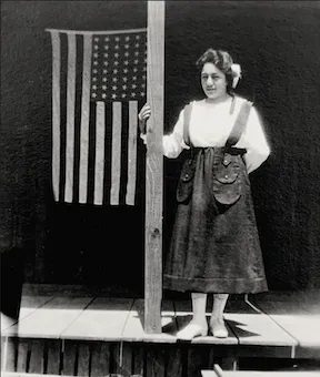 A young woman, possibly a volunteer, standing beside an American flag, April  20, 1919.
