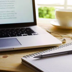 Photo of a laptop and a writing pad and pen.