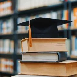 Photo illustration of a mortarboard on top of books, symbolizing academics.