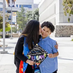 Cristal Vasquez, Class of 2023, social work, in her cap and gown holding her mortarboard and her son.