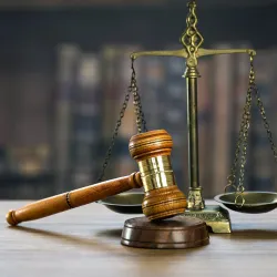 Illustration of a scale and gavel representing justice, against a dark background of books.