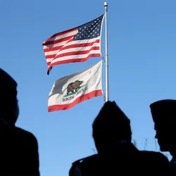 Shadows of military personnel stand near an American flag