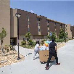 Move-in day photo of two people pushing a cart in front of a CSUSB dorm.