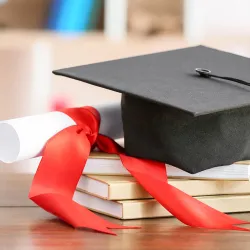 Photo of a mortarboard and rolled up paper and books illustrating education.