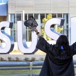 Student celebrating graduation at the CSUSB spirit letters.