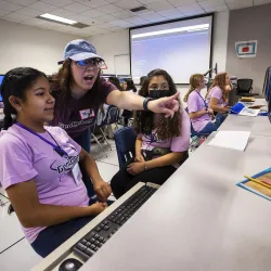Two Girl Scouts (seated) and their cybersecurity camp instructor at a computer.