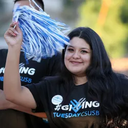 Woman wearing a Giving Tuesday T-shirt while waving a CSUSB pom pom. 