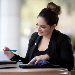 Woman sitting at a table in front of Jack H. Brown College looking through papers