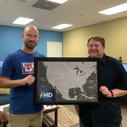 Brian Esser (left) and Kelly Schoenfeld hold up a map of the U.S. with pins in every city where their customers are using their Lightning MD software.