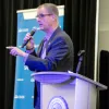 University Advancement presenter speaking at the podium during the Process Improvement & Lean Operations (PILOT) Year-End Showcase, presenting the team's Lean Six Sigma process improvement project.