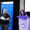 Members of the Strategic Enrollment Management and Marketing Team "One Stop Shop" presenting their process improvement project at the Process Improvement & Lean Operations (PILOT) Year-End Showcase, with one team member speaking at the podium while another stands nearby.