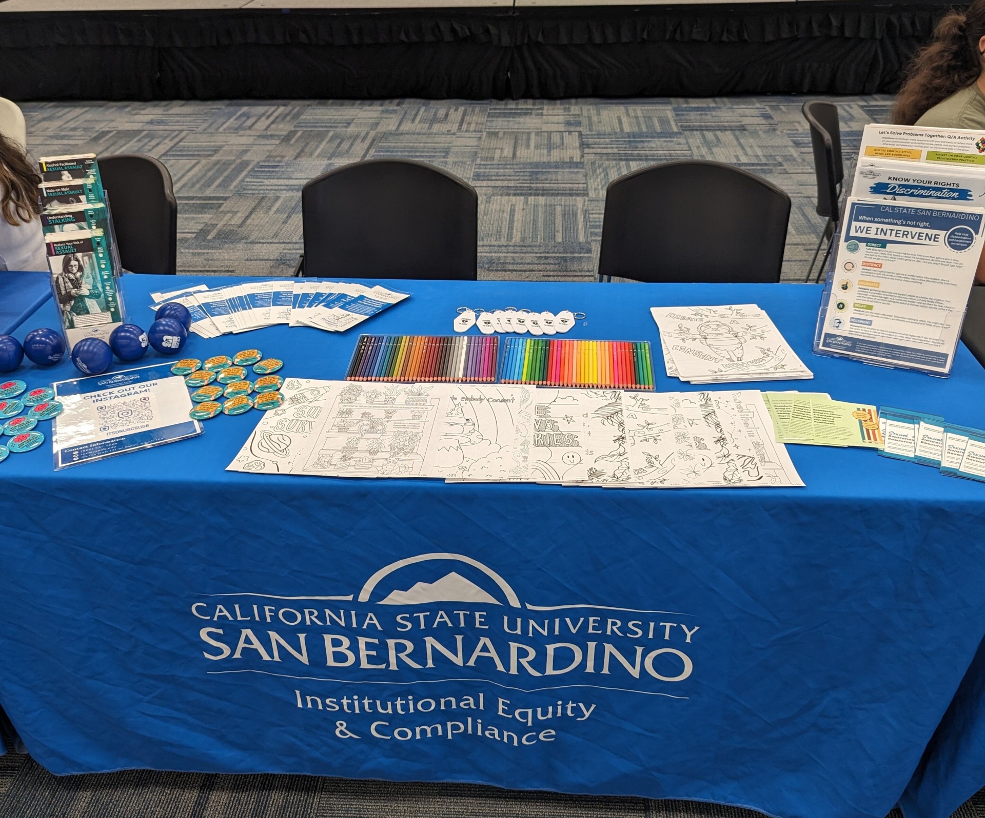 Table at resource fair, with coloring pages, swag items, and educational materials. Tablecloth reads "Institutional Equity and Compliance"