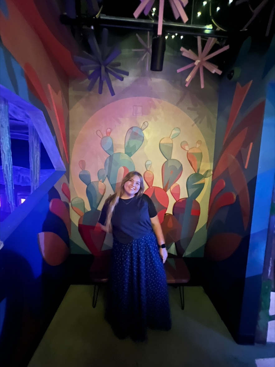 Erika Kelley smiles in front of artwork featuring a cactus