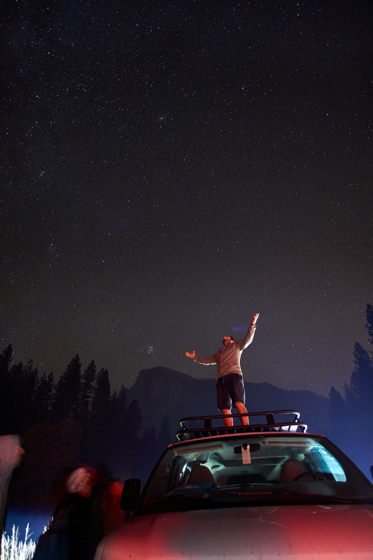 man standing on top of van with arms raised at night