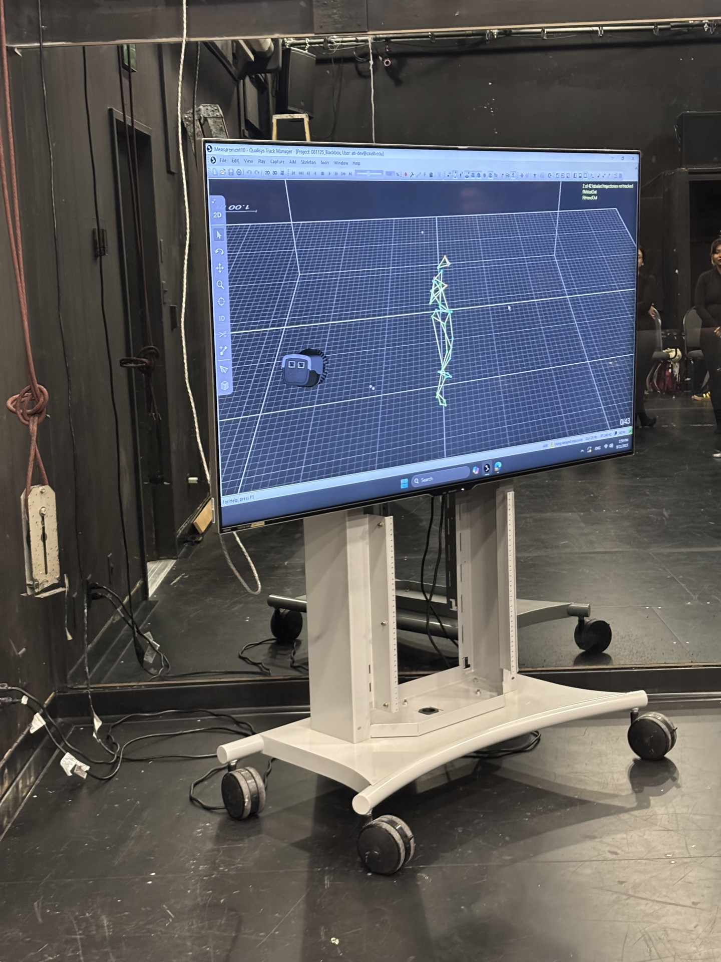 A large monitor on a rolling stand displays 3D motion capture data inside CSUSB’s Motion Capture Studio, showing a wireframe human figure in Qualisys Track Manager software as part of a live capture session.