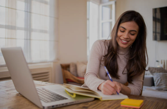 student writing on notebook in front of laptop