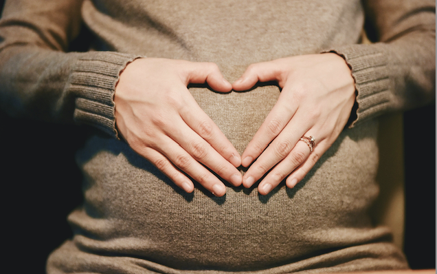 Women covering her pregnant stomach with hands forming a heart.