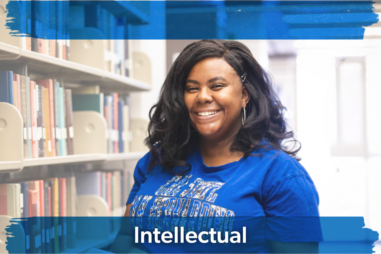 Smiling person stands in a library wearing a blue shirt. Books on shelves are in the background. The image conveys a cheerful, intellectual mood.