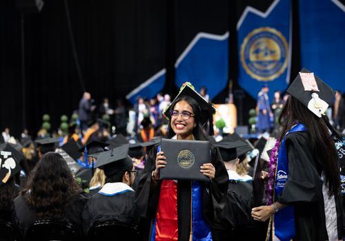 Student is holding a CSUSB diploma and graduating.