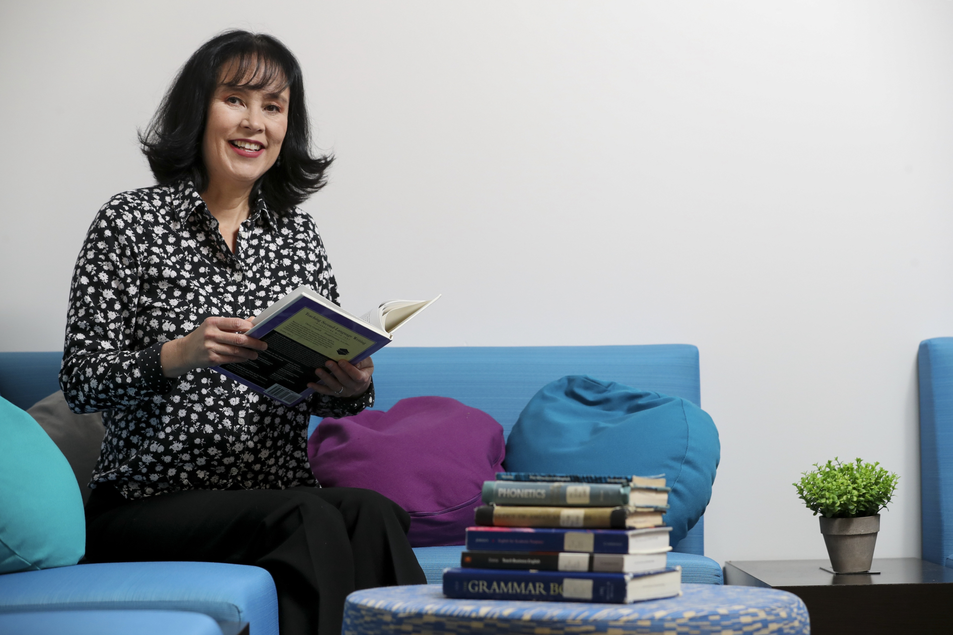 Image of Dr. Sunny Hyon sitting on a blue couch holding a book and smiling