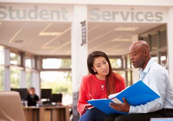 Student meeting with a financial aid counselor. A notebook is opened and they are both looking at it.