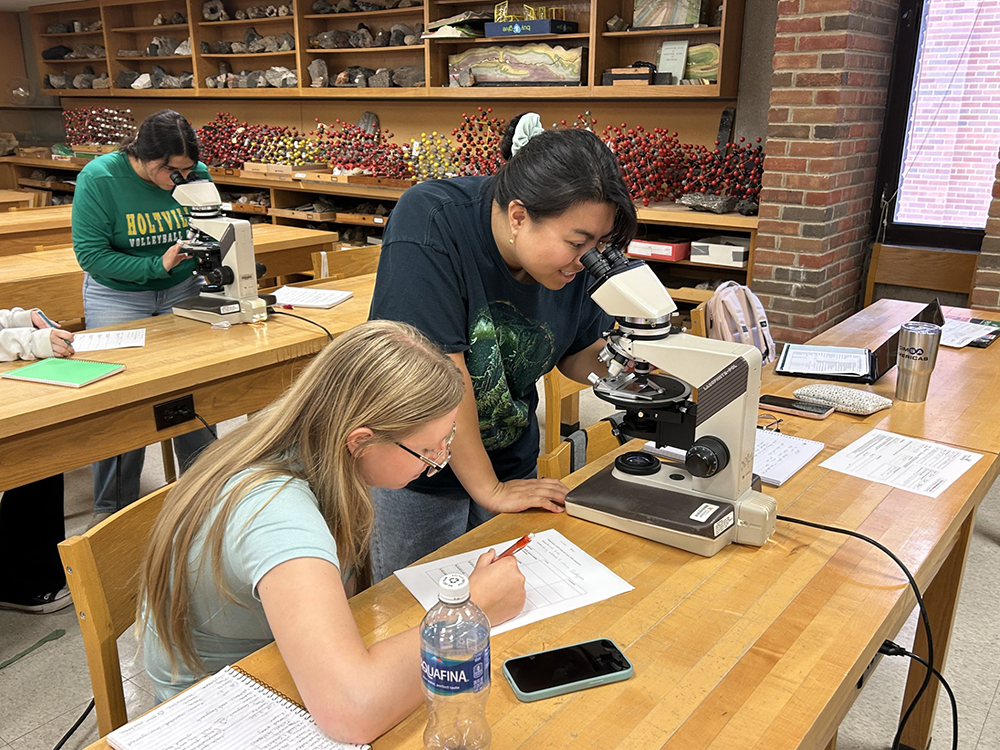 CSUSB students Emily Mackenzie and Johanna Quidangen examine sandstone slices under a microscope in a University of Cincinnati classroom. By counting tiny mineral grains, they piece together clues about past landscapes and how the rocks originally formed.