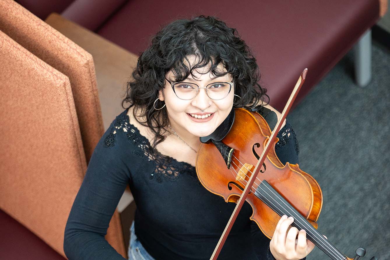 A student musician plays the violin as she looks up from one of the lower level student lounges in the new Performing Arts Center.