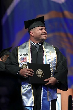 Student at Commencement holding diploma cover, wearing veterans sash
