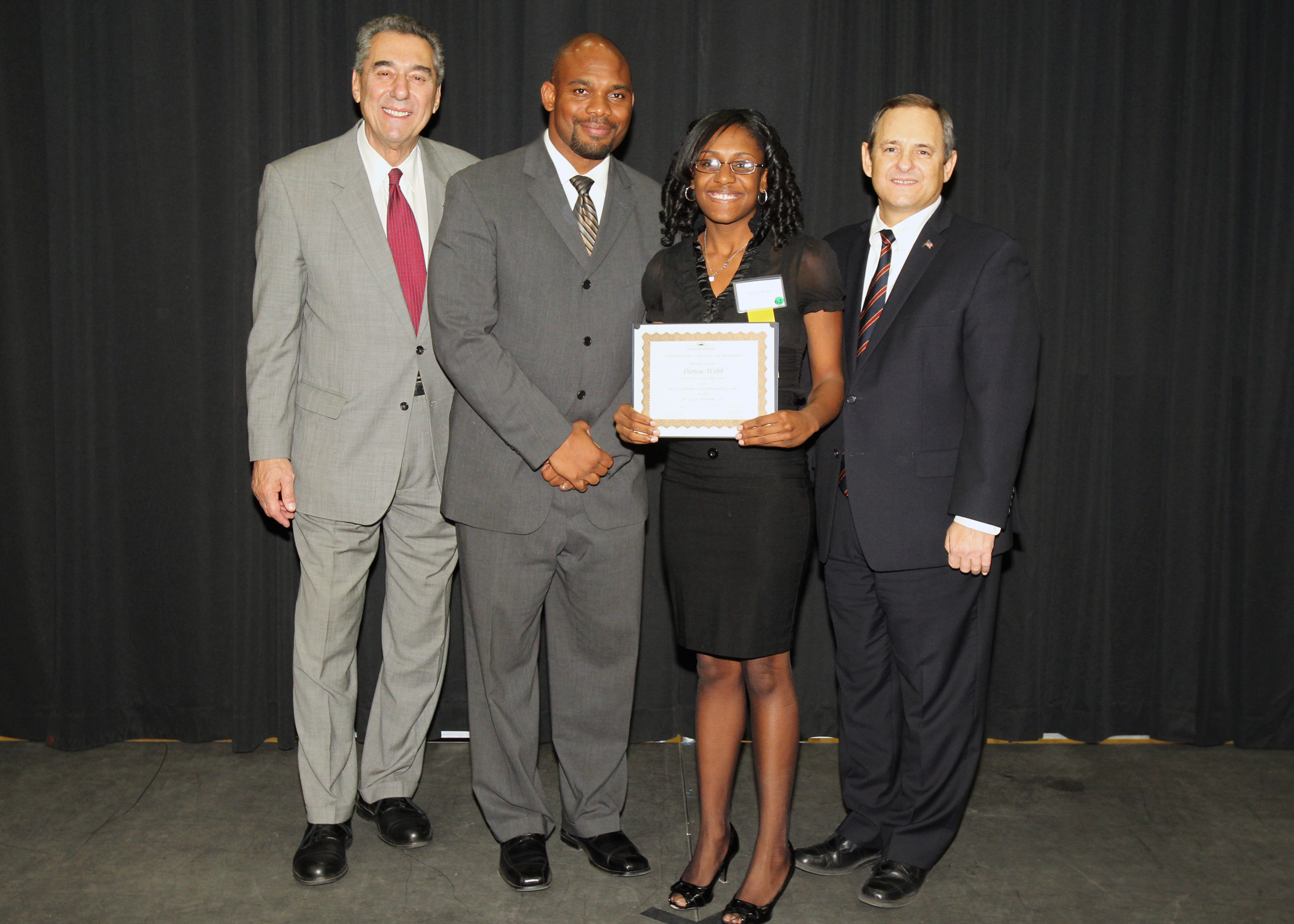 Administrators standing with student receiving a certificate.