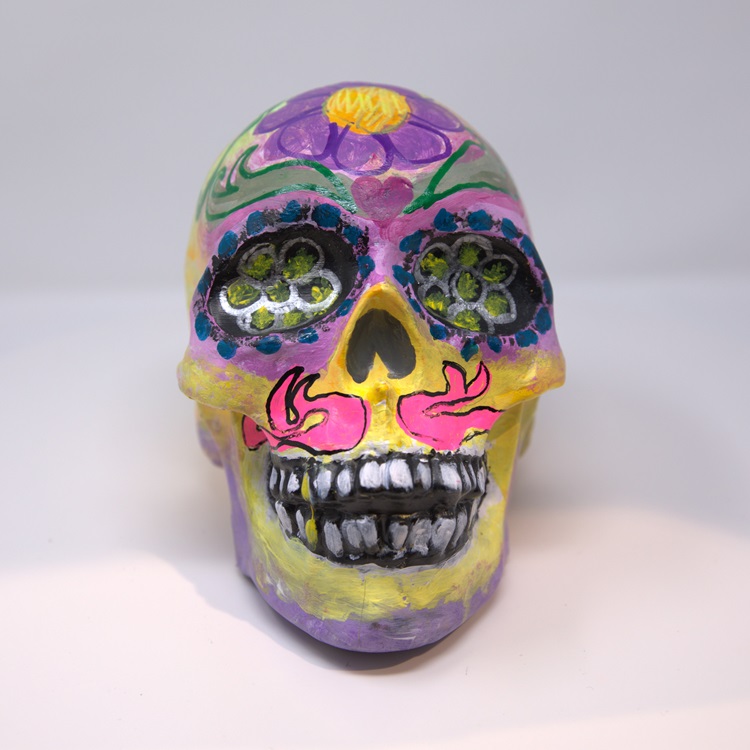 Colorful calavera with pink, purple, yellow and green flower and flame details.