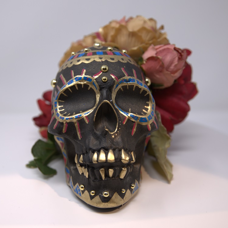 Black painted skull with gold, blue and red details, gold embellishments and a flower crown
